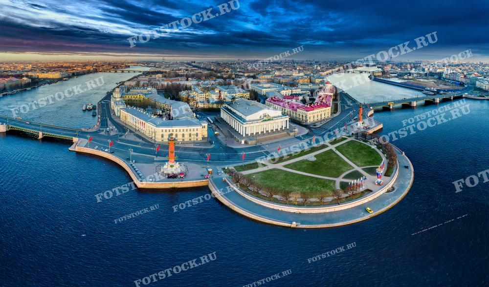 Этот захватывающий панорамный вид с дрона показывает Стрелку Васильевского острова в Санкт-Петербурге на рассвете. На фотографии видны Ростральные колонны, Биржа и другие здания на фоне утреннего неба и спокойных вод реки Невы. Идеально подходит для использования в туристических путеводителях, культурных и исторических публикациях, а также может заинтересовать фотографов и историков.